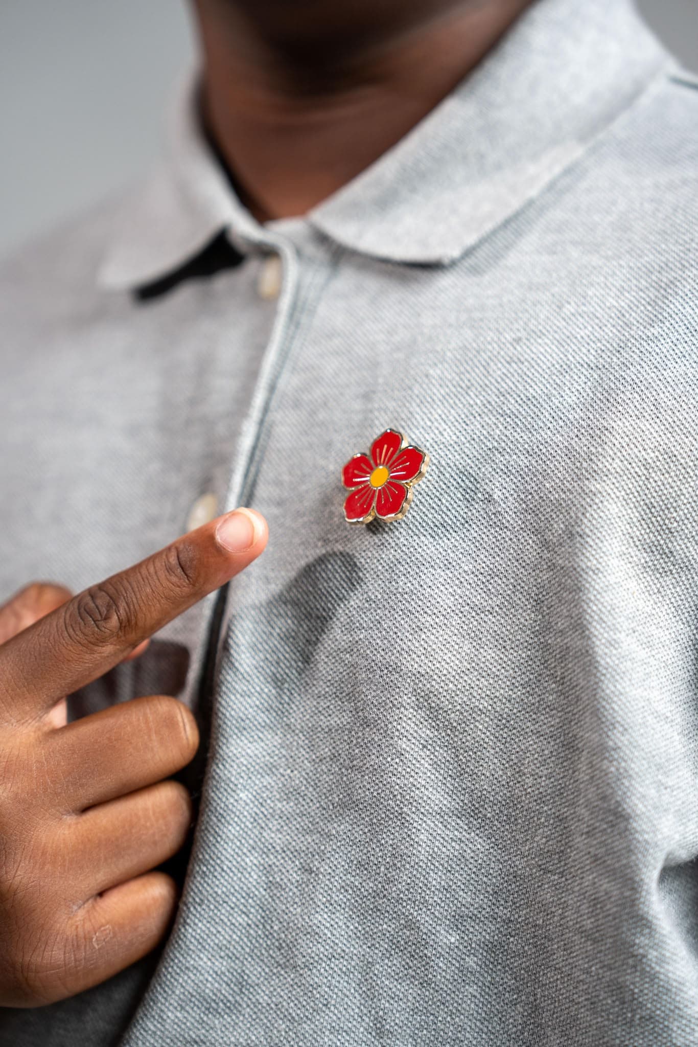 Personne portant l’Hibiscus du Courage épinglé sur un polo gris.